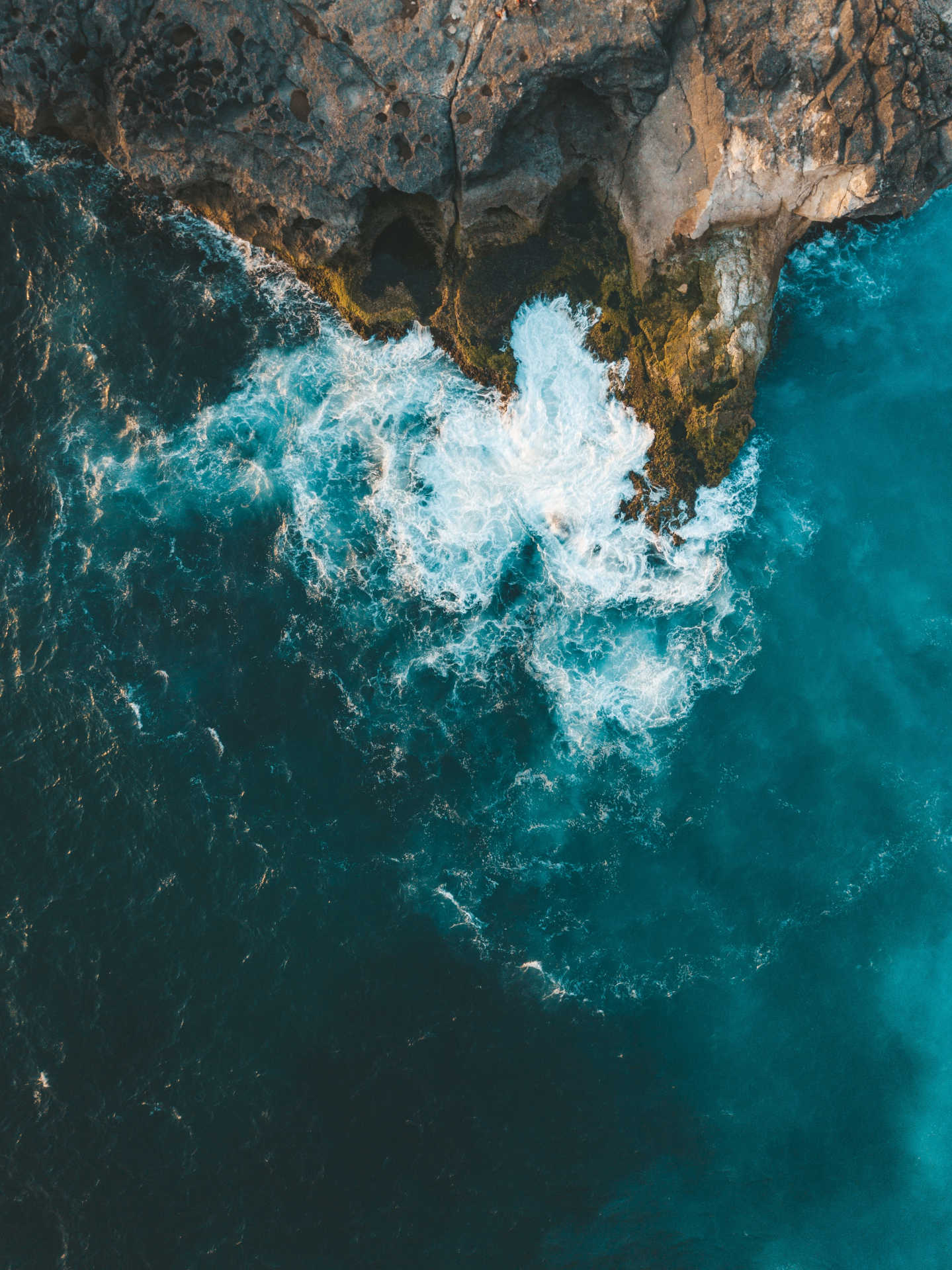 Vertical aerial shot of sea waves hitting the cliff